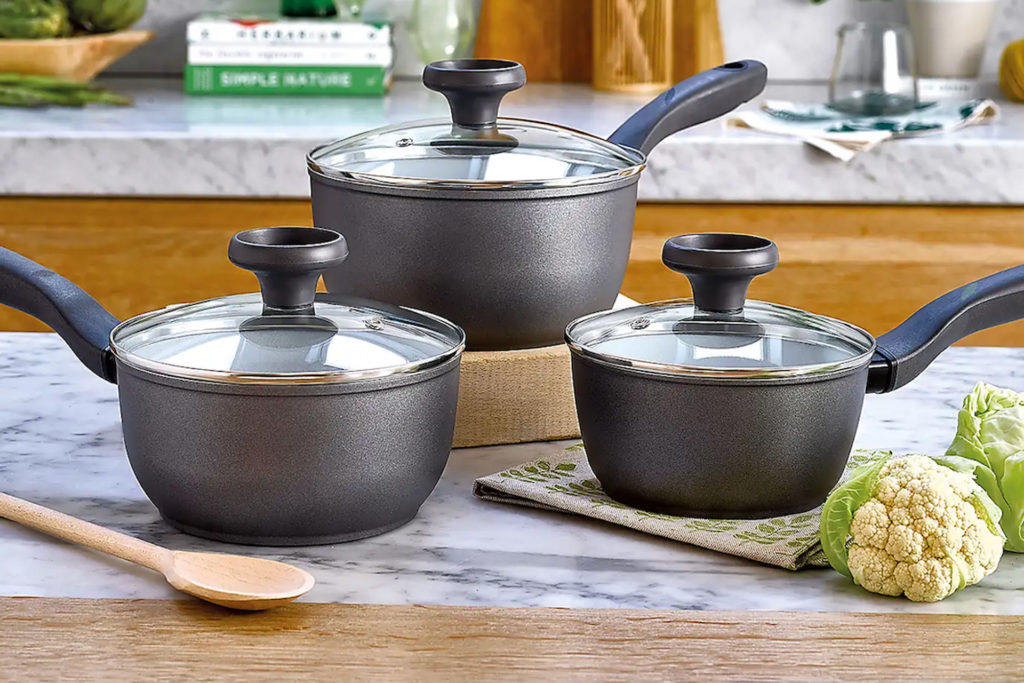 Grey saucepans on counter with vegetables and wooden spoon beside