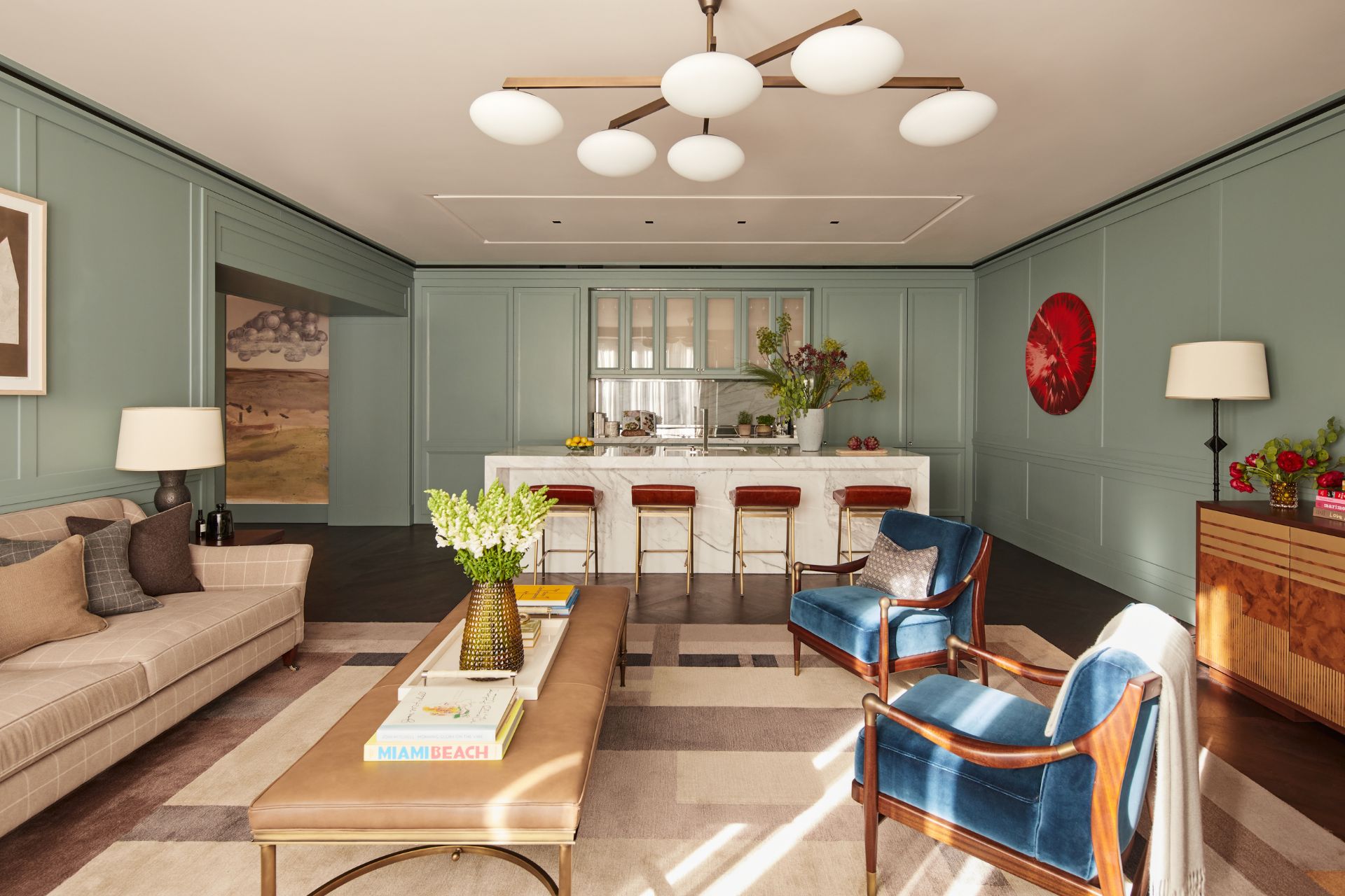 Mayfair apartment with pale green walls, blue velvet armchairs and a white marble kitchen island with red bar stools