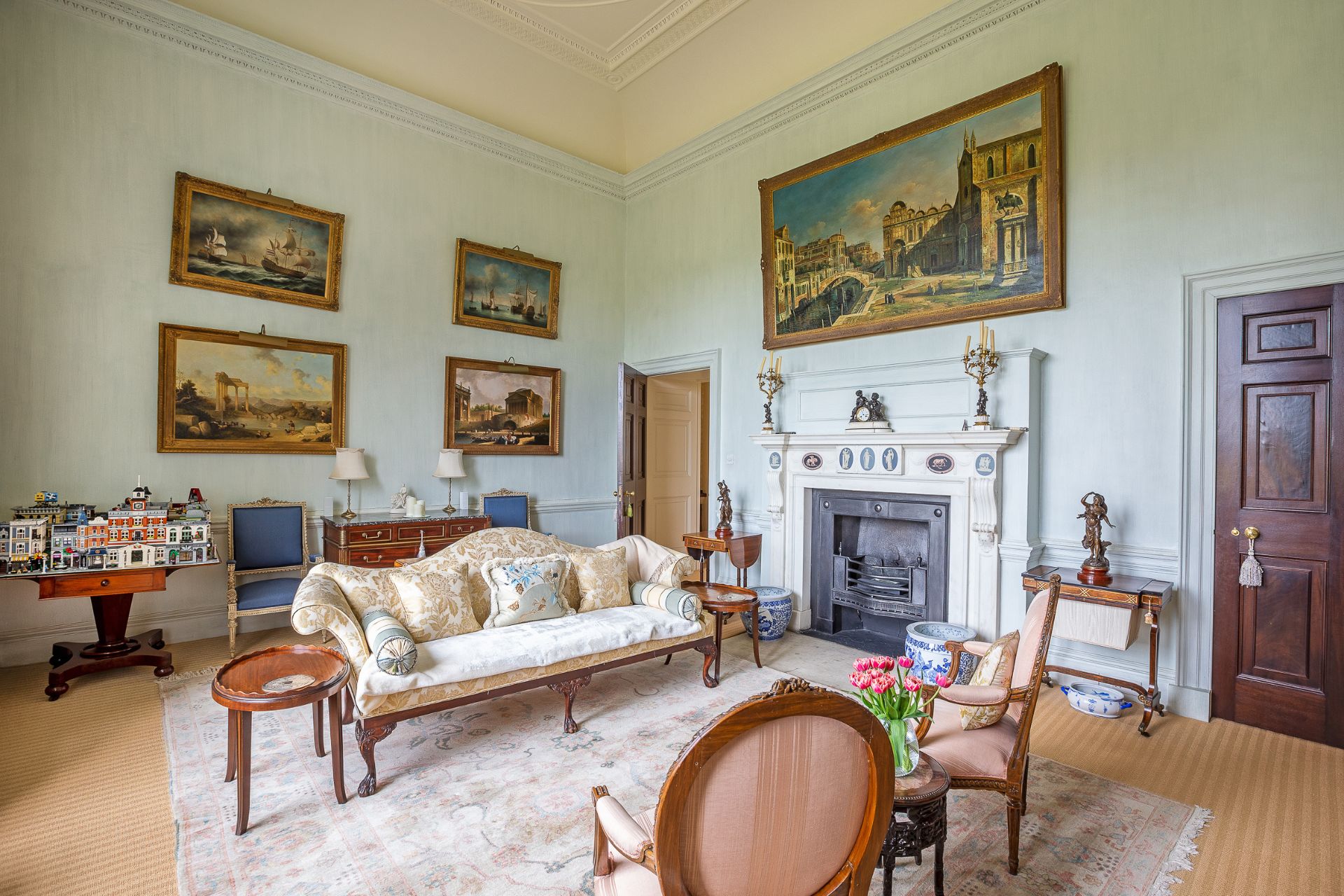 Living room with pale blue walls, marble fireplace and gilded picture frames