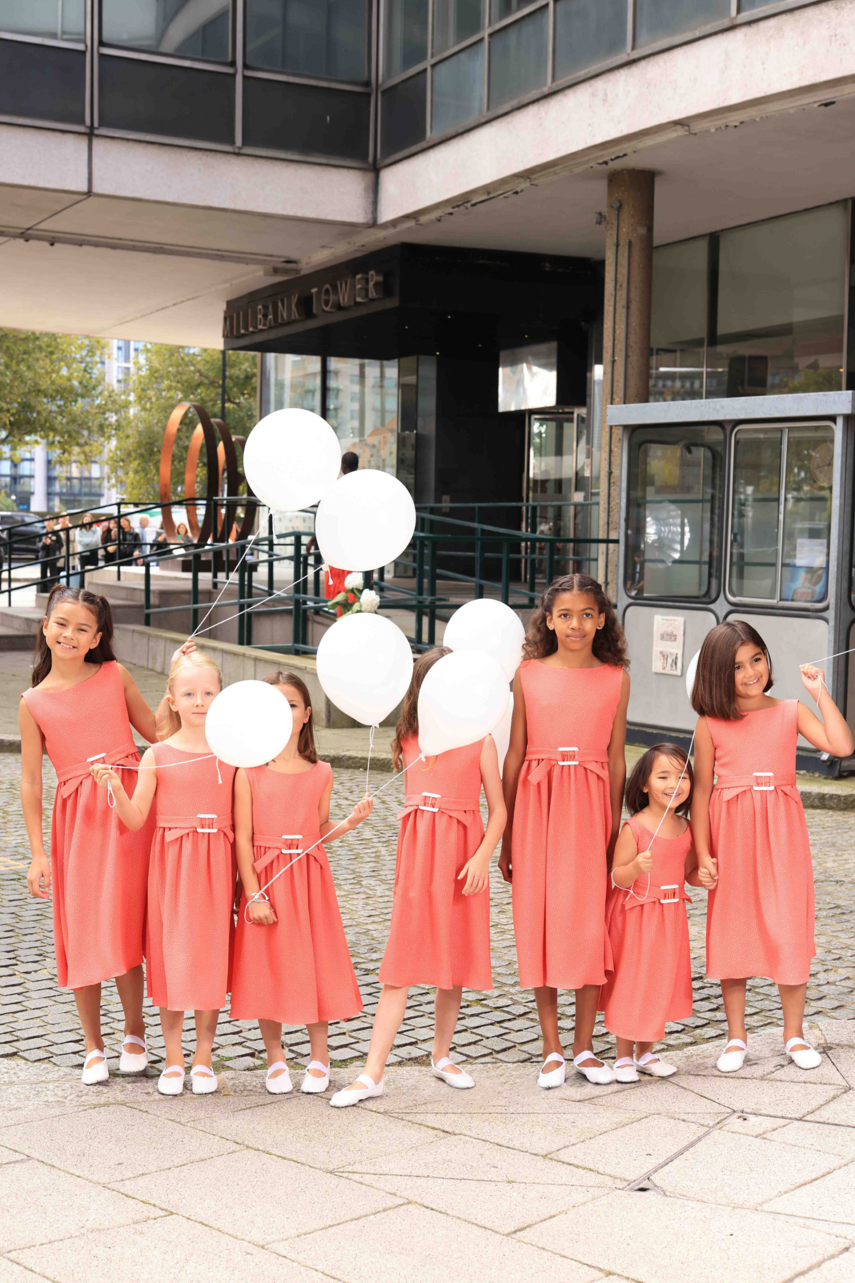 Children wearing pink dresses holding white balloons