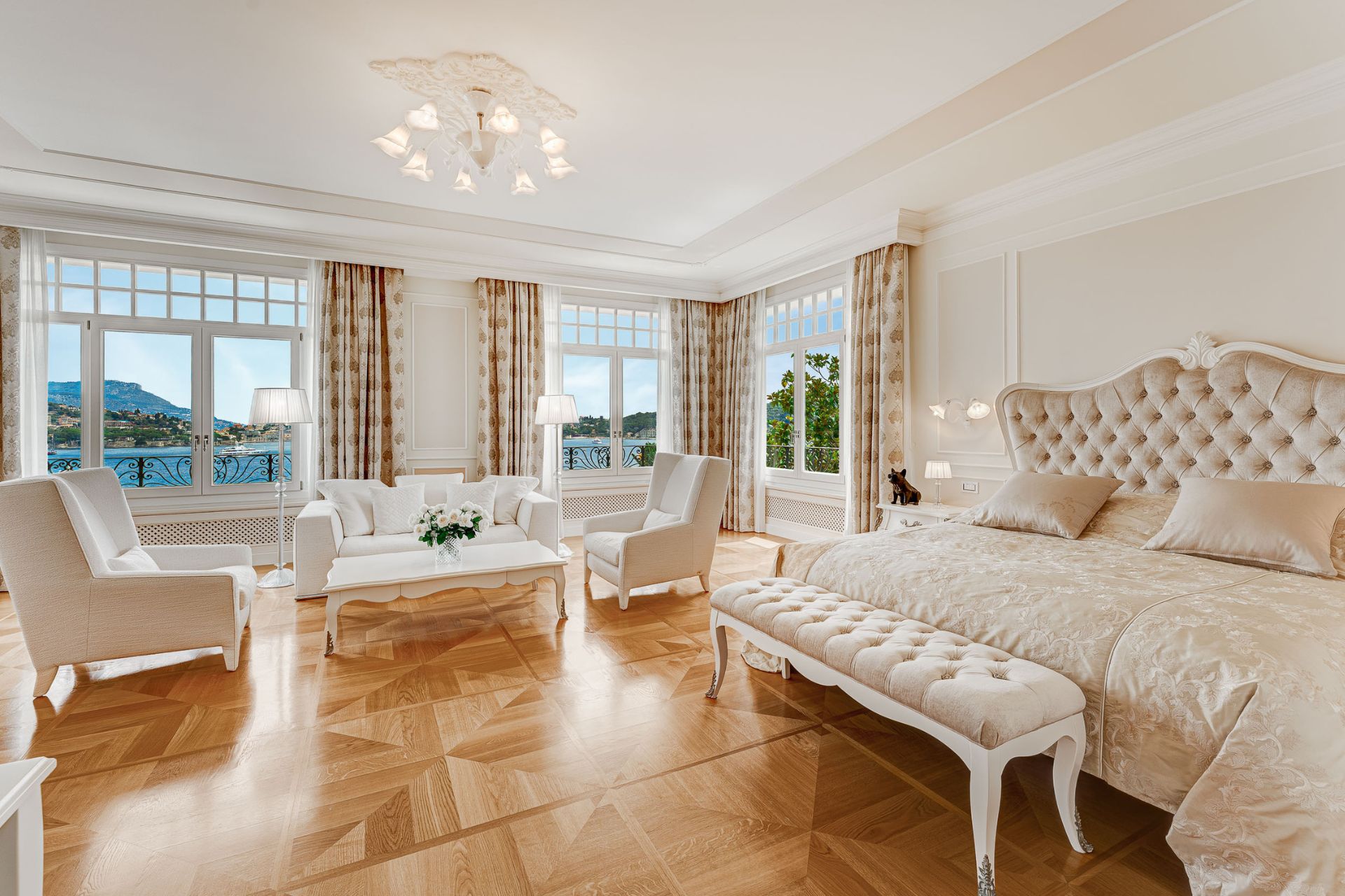 Bedroom with white furniture, parquet floors, a large bed with a white chaise longue, and views of the French Riviera.