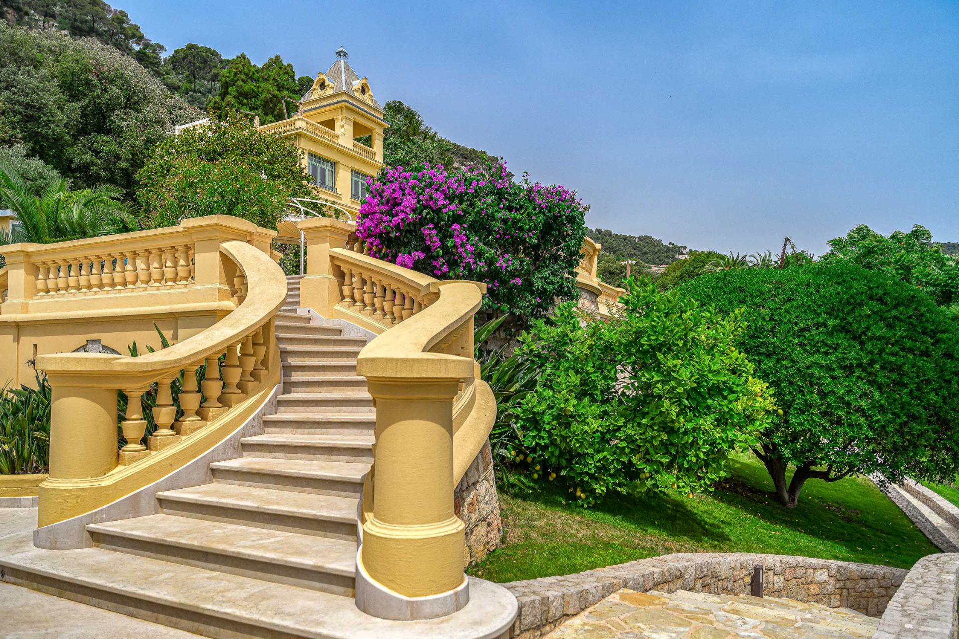Winding staircase leading to a large villa surunded by trees and purple flowers.