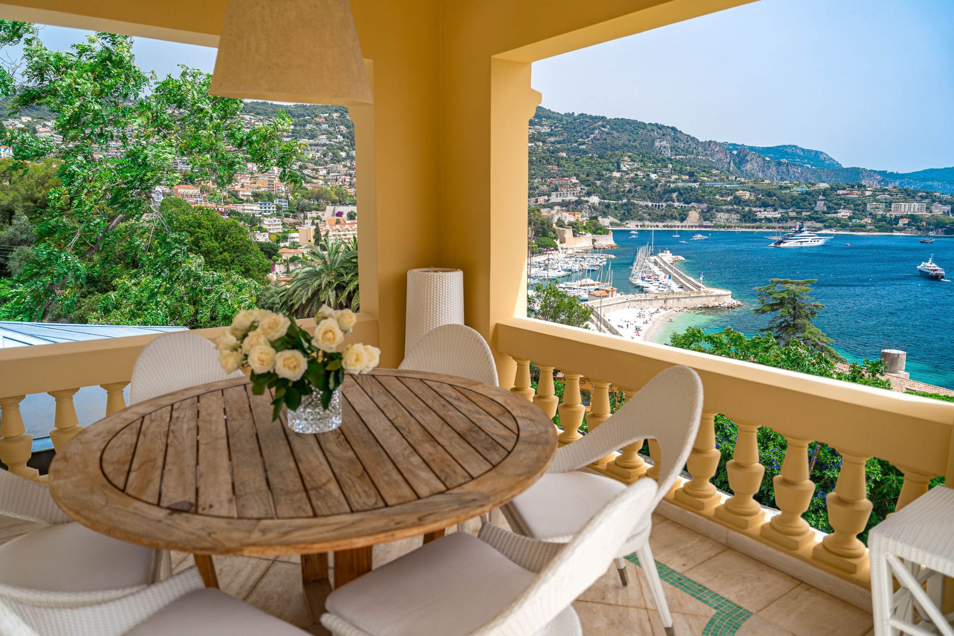 Roof terrace with a circular wooden table, white chairs and views of the Mediterranean.