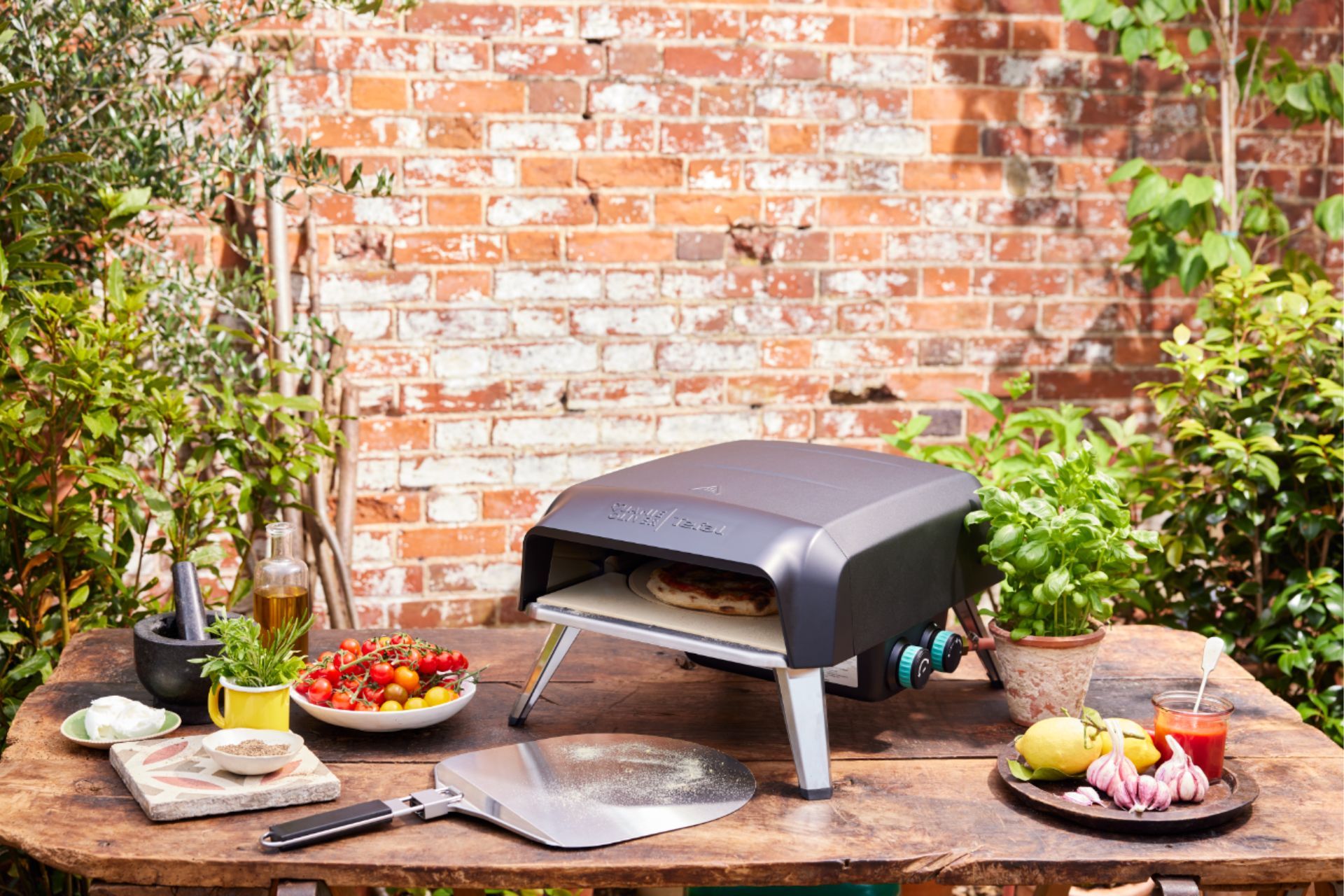 Pizza oven on a wooden table against a brick garden wall